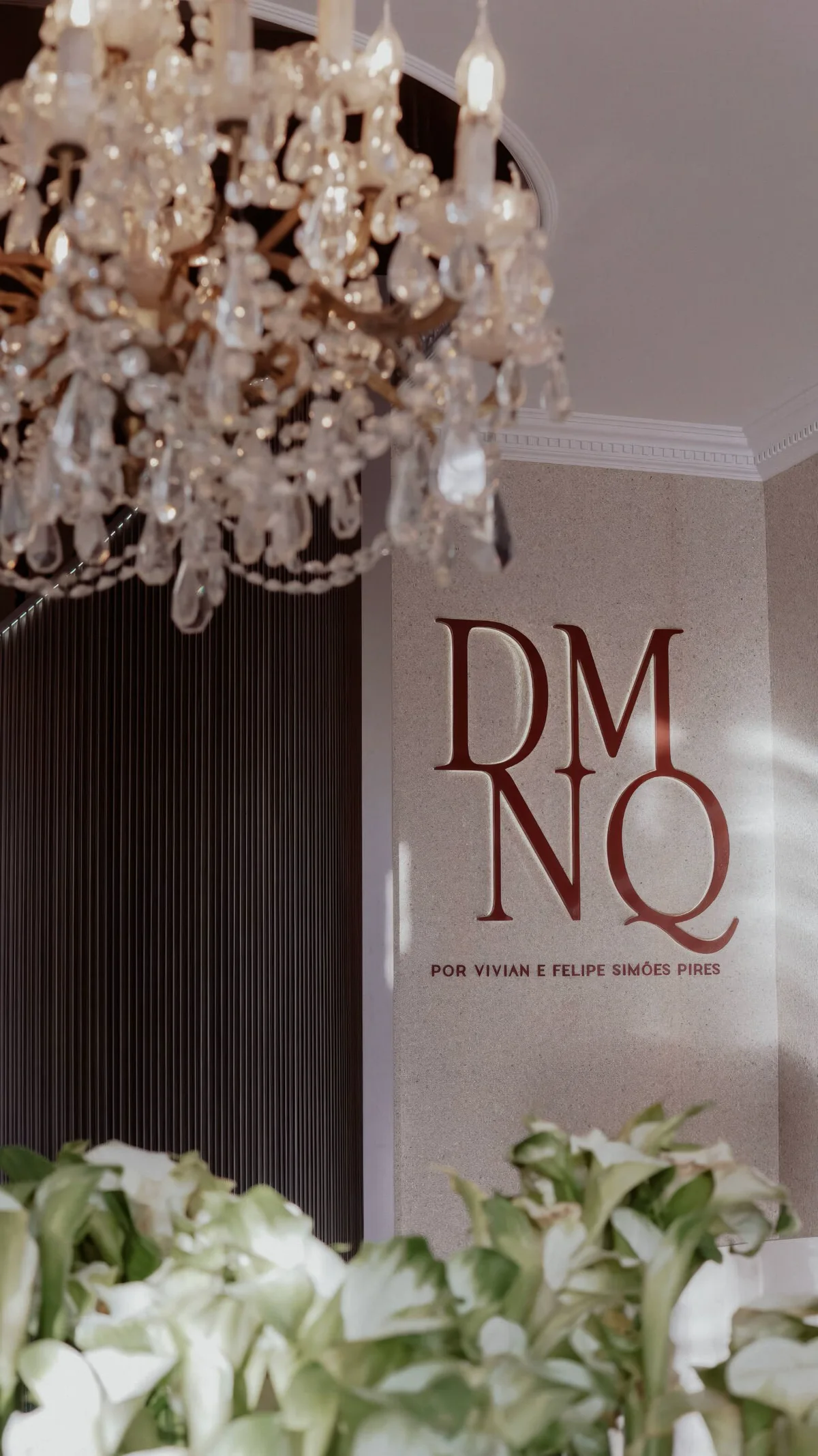 Placa DMNQ por Vivian e Felipe Simões Pires, sob um lustre de cristal