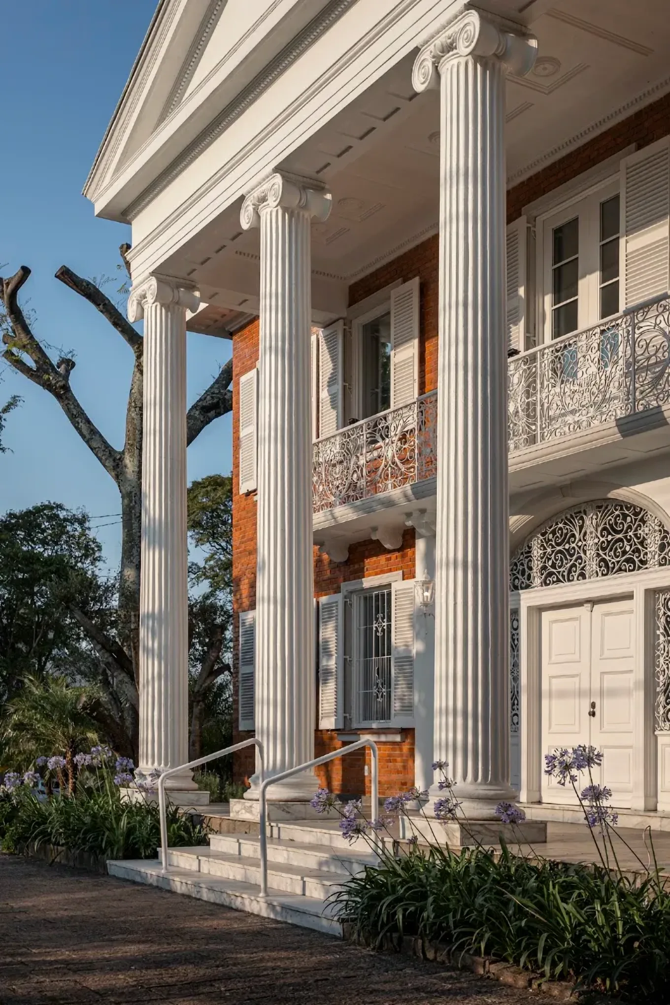 Colunas do pórtico do casarão da Dominique, com a escada de entrada e o jardim